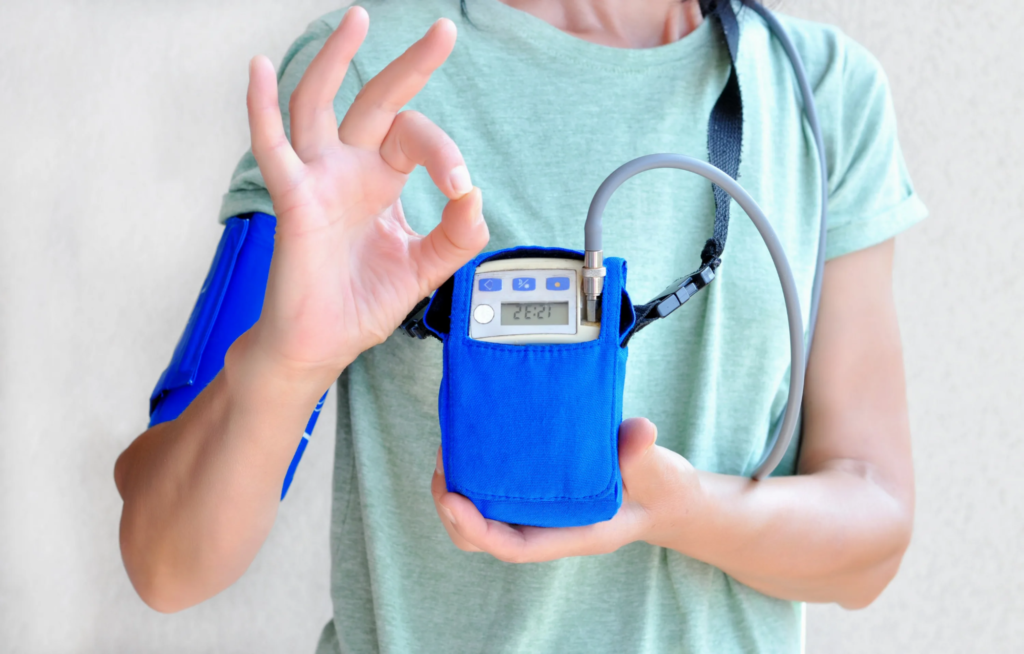 Person demonstrating a blood pressure monitor while making an okay hand gesture.